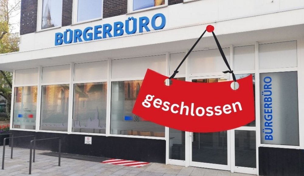 Außenansicht des Bürgerbüros der Stadt Viernheim. Über der breiten Fensterfront des Gebäudes befindet sich der große blaue Schriftzug „BÜRGERBÜRO“. Rechts ist der verglaste Eingangsbereich mit einer weißen Doppeltür zu sehen. Daneben steht der Schriftzug „BÜRGERBÜRO“ nochmals senkrecht in blauen Buchstaben. Auf mehreren Fensterscheiben sind das Logo der Stadt Viernheim und stilisierte Gebäudeansichten abgebildet. In den Scheiben spiegeln sich die gegenüberliegenden Gebäude, darunter eine Kirche. Vor dem Eingang erstreckt sich ein gepflasterter Vorplatz mit mehreren schwarzen Metallbügeln.